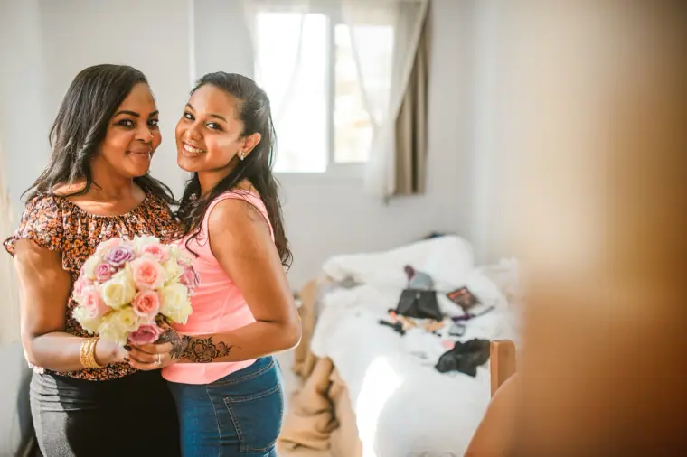 Two smiling women holding a pastel rose bouquet in the bridal suite