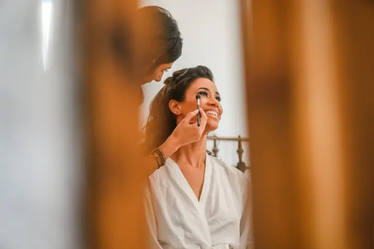 Bride dabbing on make-up, framed by a blurred wooden door