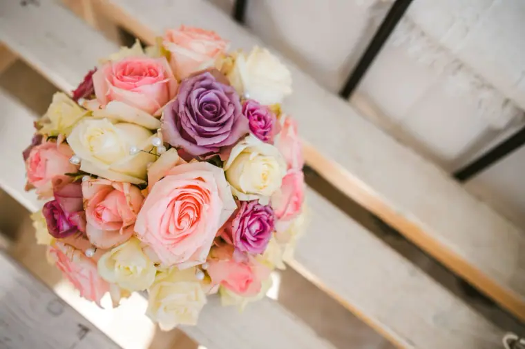 Bridal bouquet of pink, purple and cream roses on white wooden slats