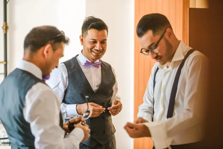 Groom in a waistcoat and purple bow tie getting ready with two groomsmen