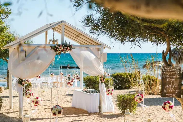 White wooden gazebo draped with fabric and flowers on the beach by the sea, Ayia Napa