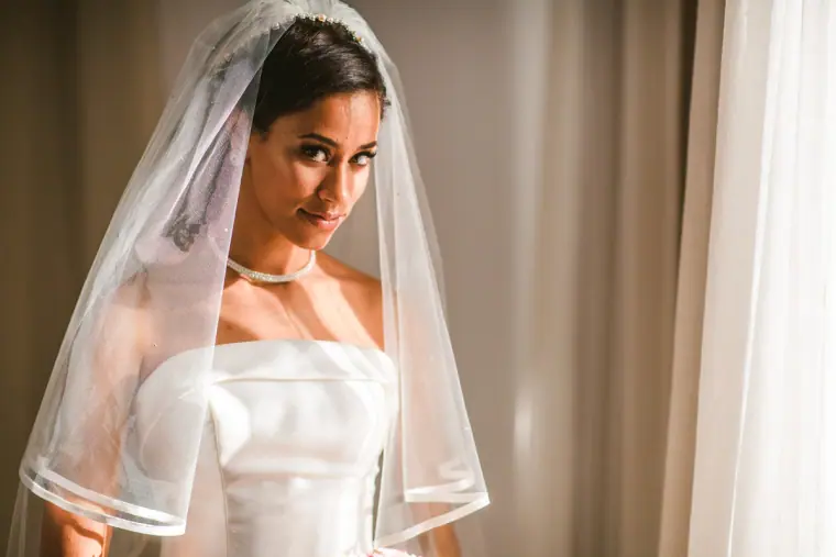 Bride in a ribbon-edged veil glancing over her shoulder in soft window light