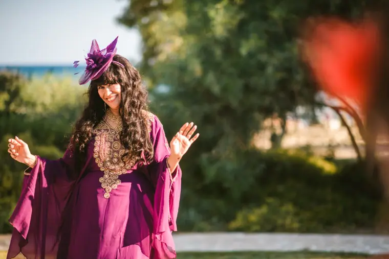 Wedding guest in a magenta embellished kaftan and fascinator in the villa garden