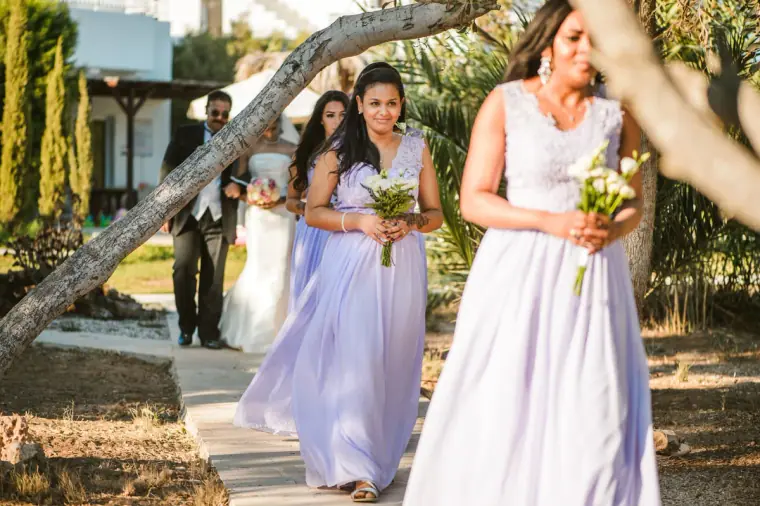 Bridesmaids in lilac gowns walking down a garden path beneath pine trees