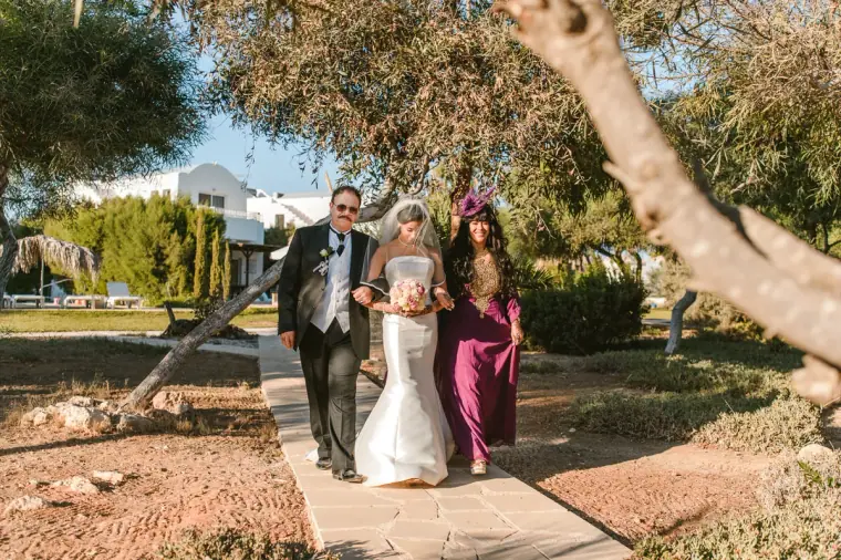 Bride walking along the path to the beach with her father and a woman in magenta