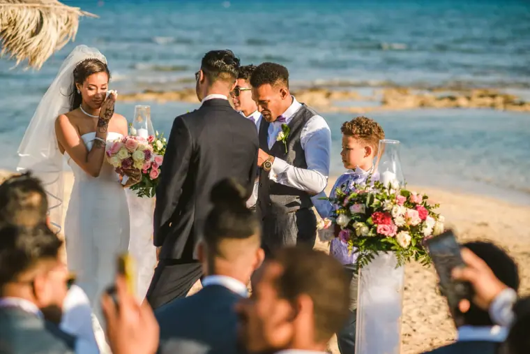 Bride and groom during their beach ceremony with the sea and guests behind