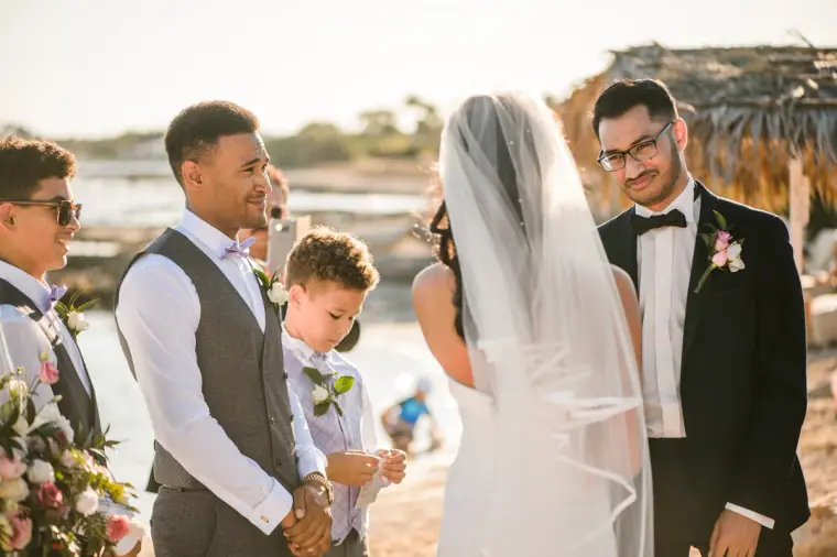 Raya and Adhib facing each other at the beachfront ceremony with groomsmen beside them