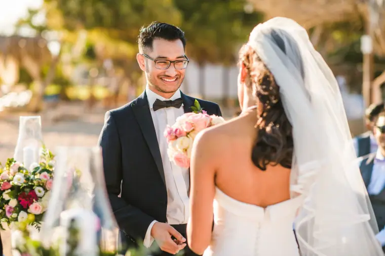 Groom smiling at the bride during the exchange of rings on the beach