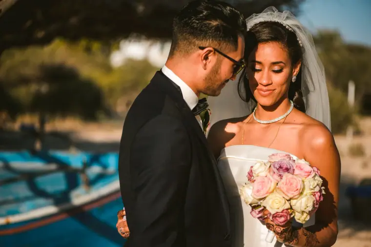 Groom resting his head against the smiling bride's beside a blue fishing boat
