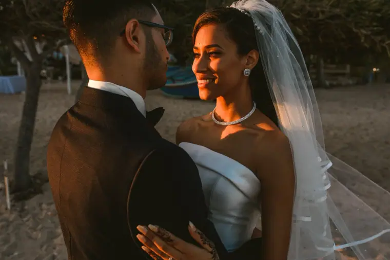 Groom holding the bride close as she smiles in warm evening light