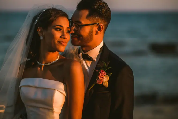 Close portrait of the bride and groom cheek to cheek with the sea behind