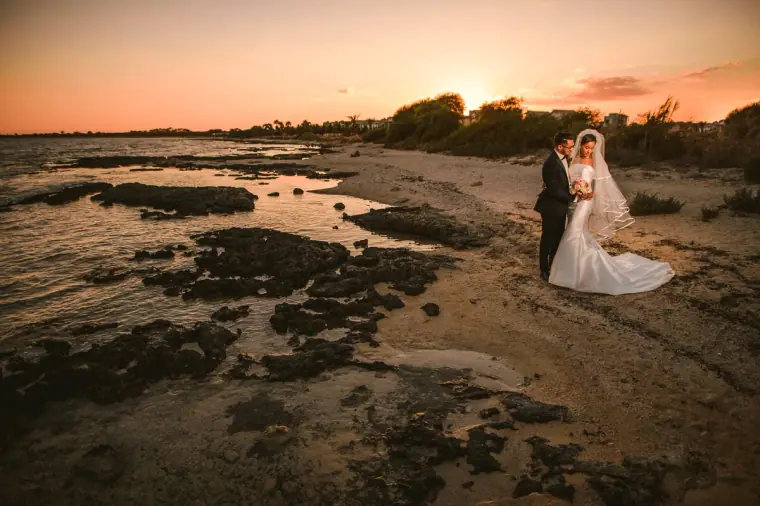Bride and groom on the rocky shore beneath a pink sunset sky, Ayia Napa