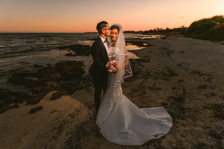 Groom kissing the bride's cheek on the shoreline in the last light of day
