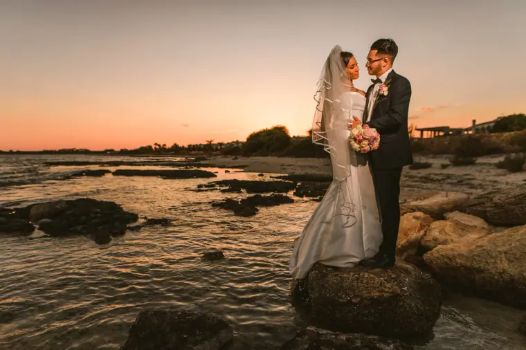 Bride and groom standing on a rock by the water at sunset, Thalassines Beach Villas