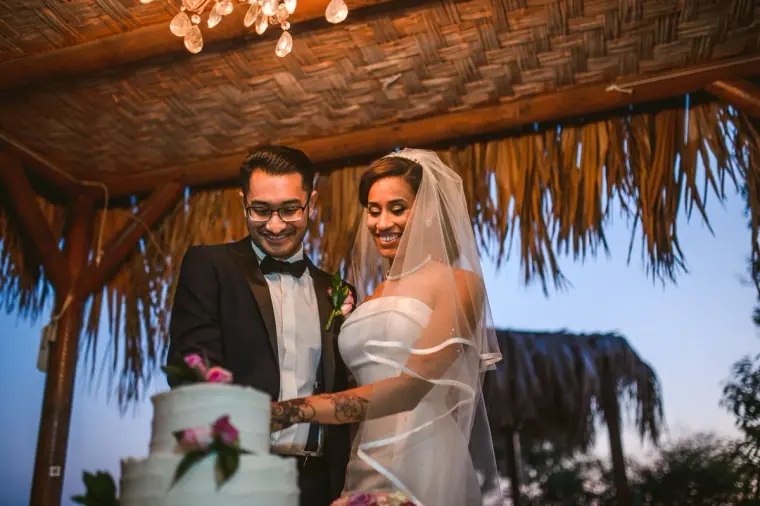 Raya and Adhib cutting their wedding cake under a thatched canopy