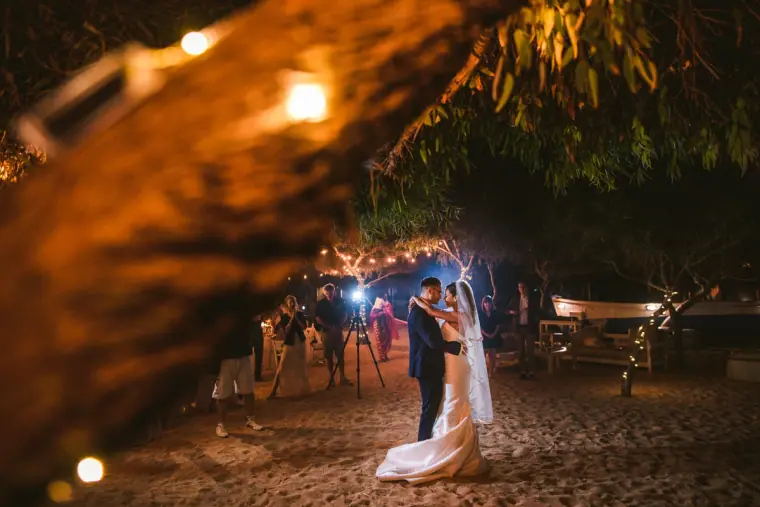 Bride and groom's first dance on the sand under pine trees and fairy lights