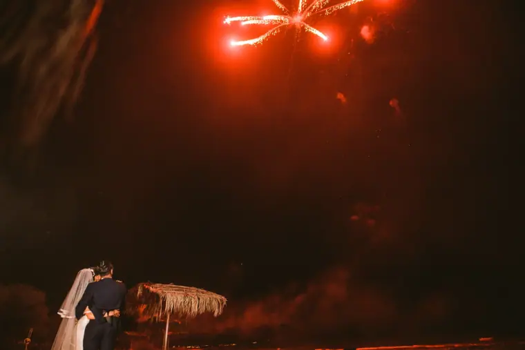 Bride and groom watching red fireworks explode in the night sky