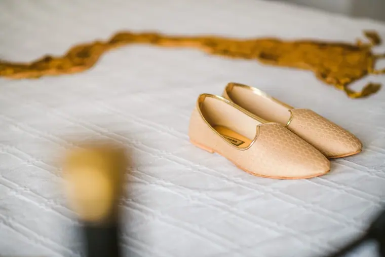 Gold embroidered slippers on a white bedspread beside a gold scarf