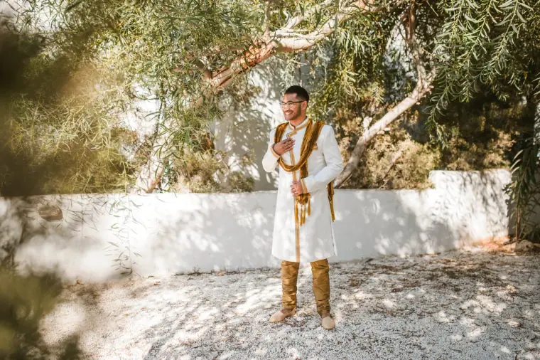 Groom in his cream sherwani standing beneath olive trees in the villa garden