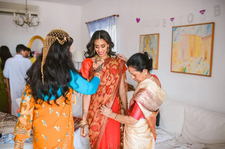 Women in colourful outfits dressing the bride in her red and gold sari