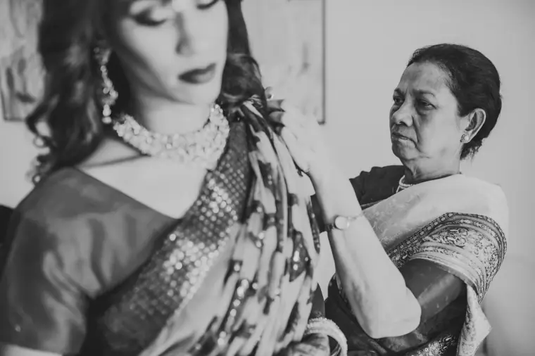 Black-and-white photo of an older woman pinning the bride's sari