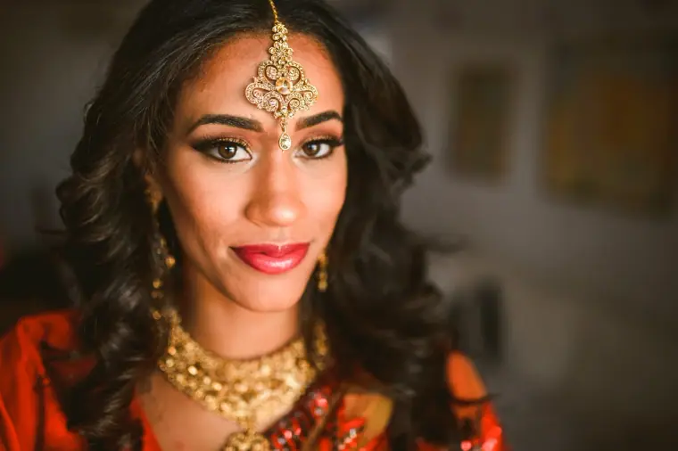 Close portrait of the bride in a gold maang tikka, choker and red lipstick