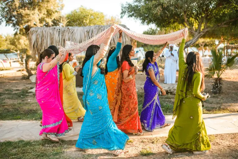 Procession of women in pink, blue, green and orange saris crossing the garden