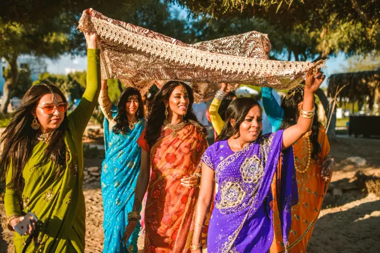 Women in saris holding the canopy high as they escort the bride through the trees