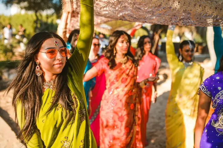 Woman in a green outfit and orange sunglasses holding up the canopy in the procession