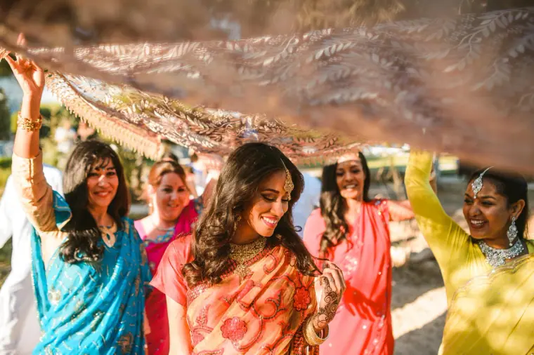 Bride laughing under the canopy with women in coloured saris all around
