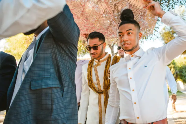 Groom in a gold scarf walking under the canopy with friends holding it aloft