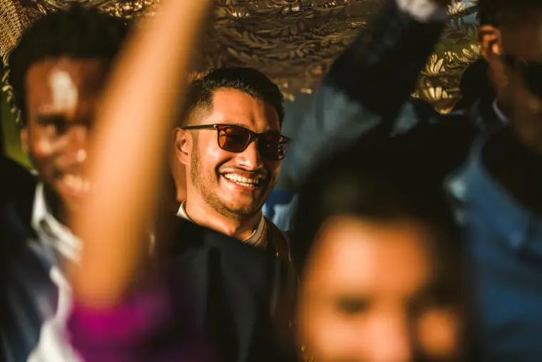 Smiling guest in sunglasses helping carry the canopy in the groom's procession