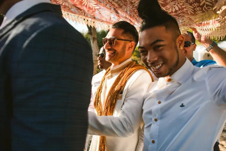 Groom and friends laughing as they hold the embroidered canopy overhead