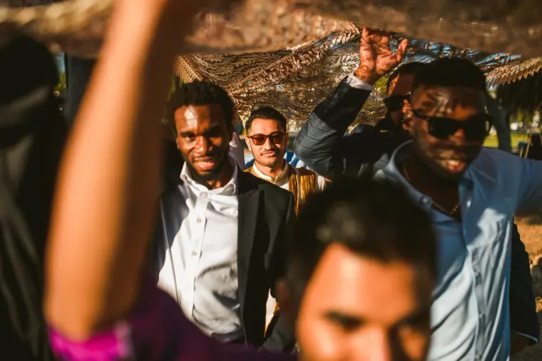 Friends in suits and sunglasses dancing beneath the canopy in the groom's procession
