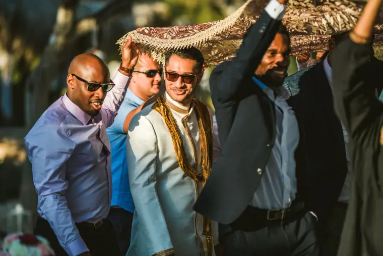 Groom in a cream sherwani and sunglasses arriving under the canopy with friends