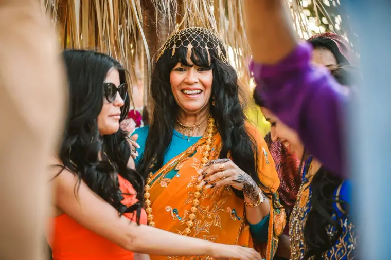 Women in orange and teal saris laughing under the thatched beach canopy