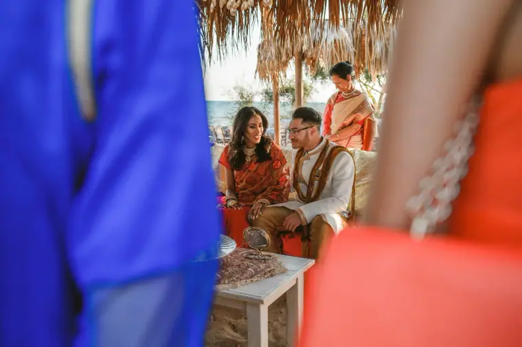 Couple seated on the red daybed under the canopy, framed by guests' colourful clothing