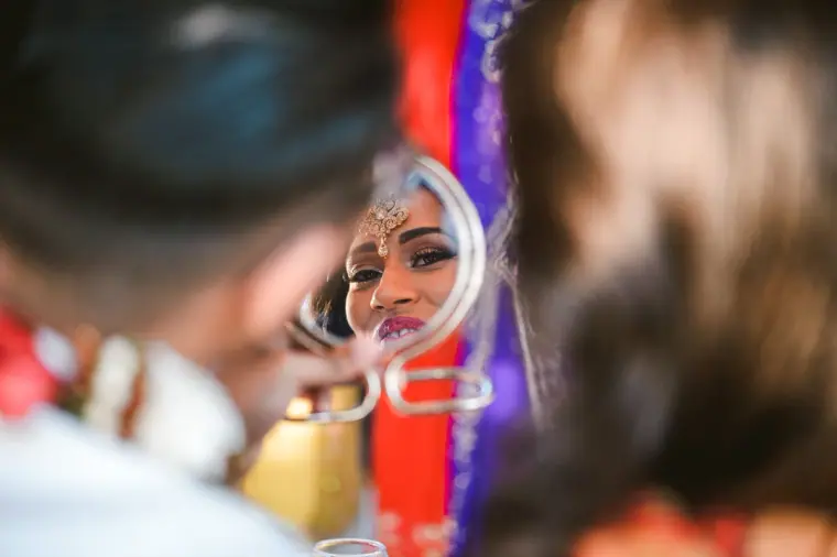 Bride's smiling reflection in a small hand mirror held up during the ceremony