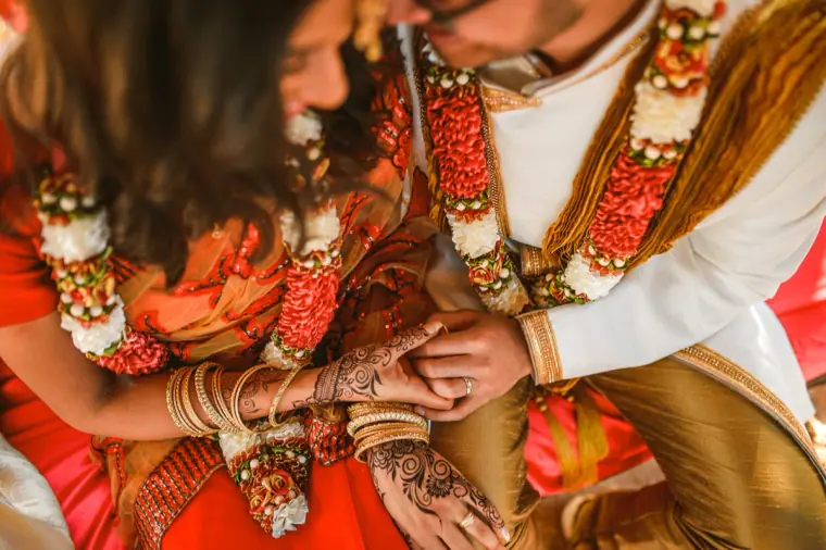 Couple in flower garlands holding hands, the bride's wrists stacked with bangles