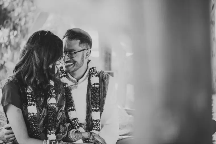Black-and-white photo of the bride and groom laughing together in garlands