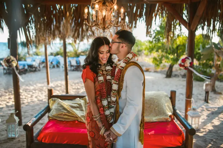 Bride and groom standing in front of the red daybed beneath the canopy and chandelier