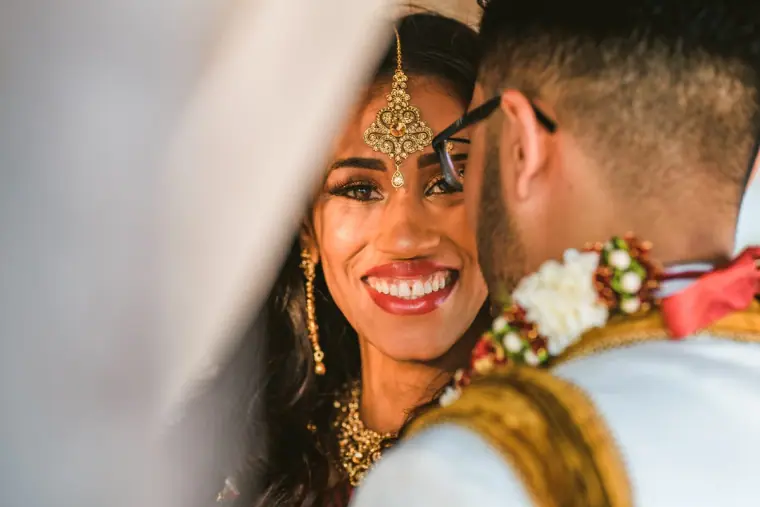 Bride in a gold maang tikka beaming as she leans against the groom's shoulder