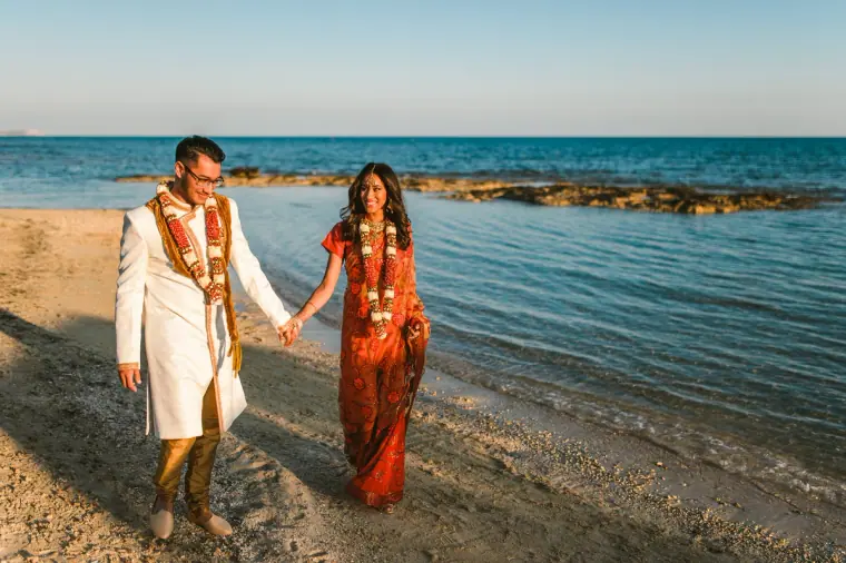 Groom leading the bride by the hand along the shoreline at Thalassines Beach Villas