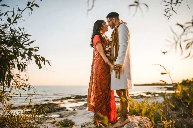 Bride and groom gazing at each other on the rocks, framed by branches