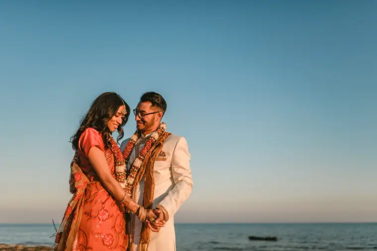 Raya and Adhib leaning together against a clear blue sky by the sea