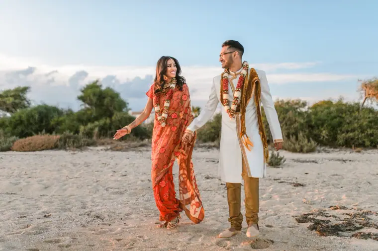 Bride and groom in traditional dress dancing on the sand at golden hour