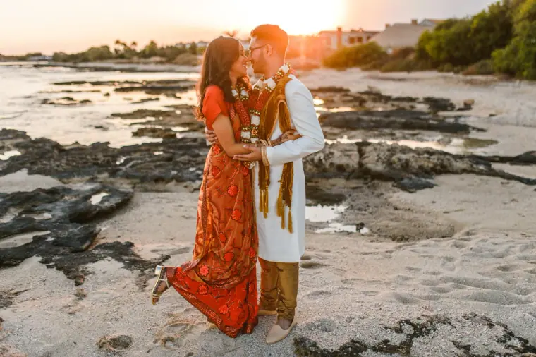 Bride on tiptoe kissing the groom among rock pools at sunset