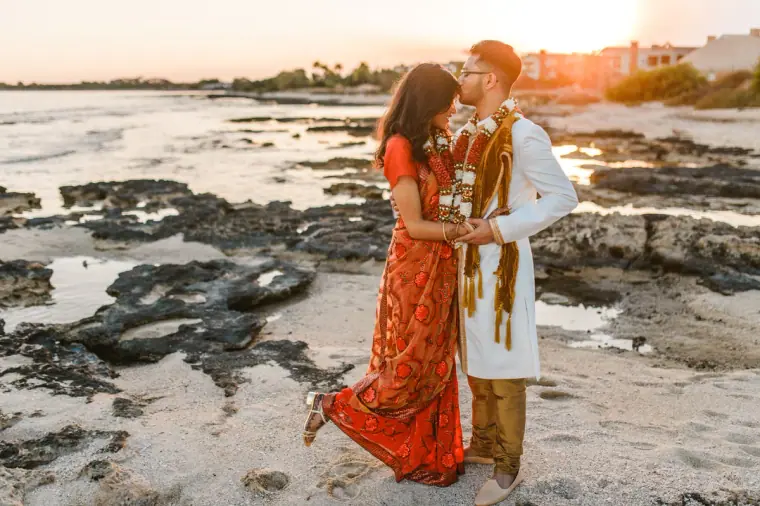 Couple in garlands kissing on the rocky beach in the evening glow
