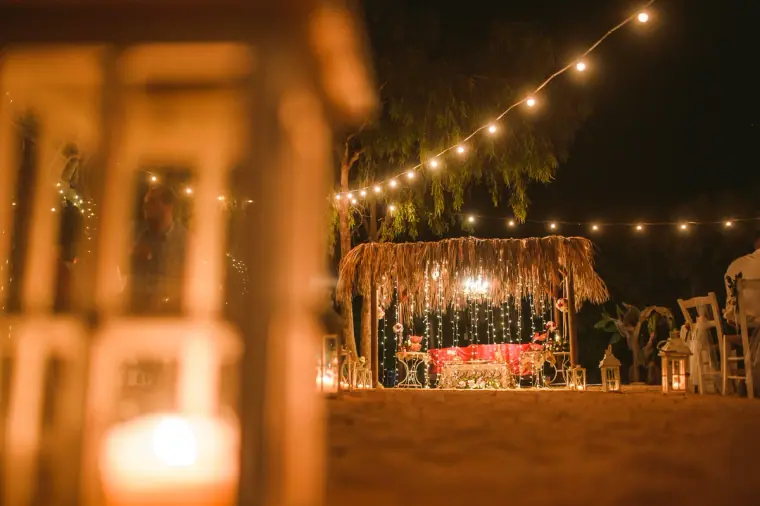 Thatched beach canopy glowing with fairy lights at night, past a lit lantern