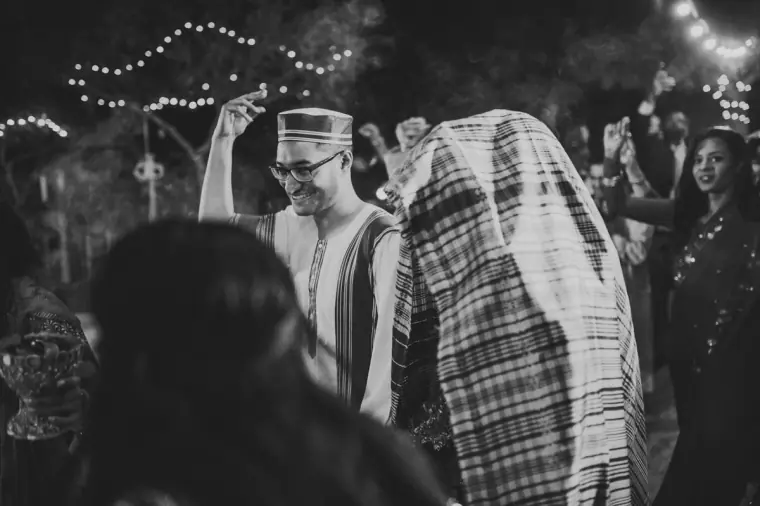 Black-and-white photo of the groom dancing among guests at night